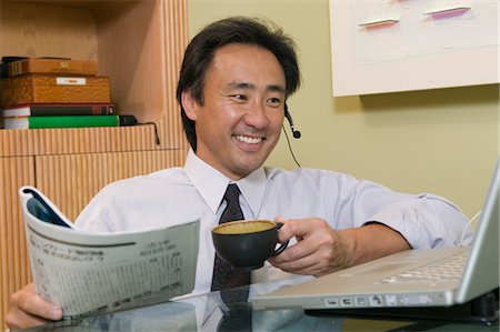 simsearch:693-03311509,k - Businessman talking on headset Using Laptop and Reading Newspaper Stock Photo - Premium Royalty-Free, Code: 693-03299403