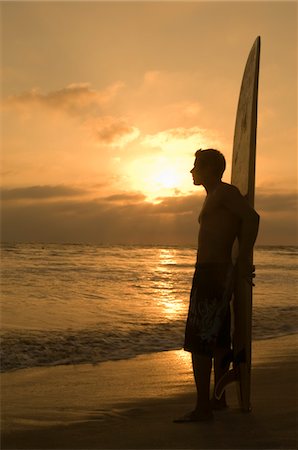 Surfer standing on beach, leaning on surfboard, watching sunset, side view Stock Photo - Premium Royalty-Free, Code: 693-03299697