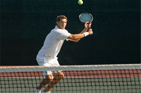 Tennis Player squatting on tennis court, Hitting Backhand over net Stock Photo - Premium Royalty-Free, Code: 693-03299728