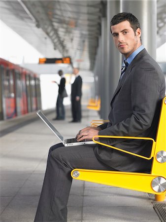 Businessman sitting on bench, working on laptop at Train Station, side view Stock Photo - Premium Royalty-Free, Code: 693-03304110