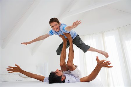 Son balancing on father's legs on bed in bedroom Stock Photo - Premium Royalty-Free, Code: 693-03304278