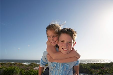 sister brother piggy back - Boy giving girl piggyback in front of ocean, half length Stock Photo - Premium Royalty-Free, Code: 693-03304282