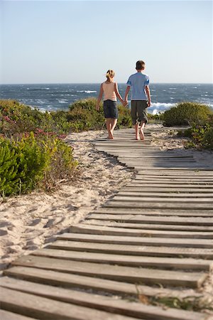 simsearch:693-03309308,k - Boy and girl walking hand in hand, along boardwalk toward sea, back view Stock Photo - Premium Royalty-Free, Code: 693-03304283