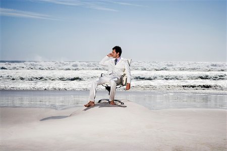 Man using mobile phone sitting on office chair on beach Stock Photo - Premium Royalty-Free, Code: 693-03304351