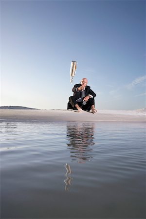 Business man sitting on beach, throwing message in bottle into sea, low angle view Foto de stock - Sin royalties Premium, Código: 693-03304364