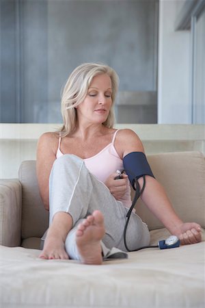 senior blood pressure - Mature woman sitting on sofa, barefoot checking blood pressure with sphygmometer Foto de stock - Sin royalties Premium, Código: 693-03304388