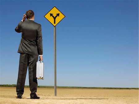 scratching head - Rear view of confused businessman looking at desert road sign Stock Photo - Premium Royalty-Free, Code: 693-03304479