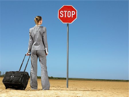 Business woman with luggage, standing in front of stop sign in desert, back view Stock Photo - Premium Royalty-Free, Code: 693-03304482