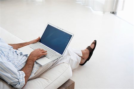 Homme utilisant un ordinateur portable, assis sur le canapé dans le salon, la partie basse, élevée vue Photographie de stock - Premium Libres de Droits, Code: 693-03304616