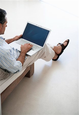 Homme utilisant un ordinateur portable, assis sur le canapé dans le salon, élevé vue Photographie de stock - Premium Libres de Droits, Code: 693-03304617