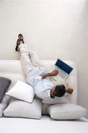 Homme utilisant un ordinateur portable, assis sur le canapé dans le salon, vue de dessus Photographie de stock - Premium Libres de Droits, Code: 693-03304619