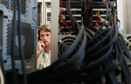 Man using phone, surrounded by computer equipment. Stock Photo - Premium Royalty-Free, Code: 693-03304661