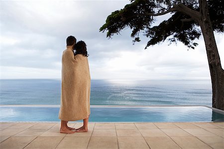 Couple covered in towel, standing by infinity pool, side view Stock Photo - Premium Royalty-Free, Code: 693-03304683