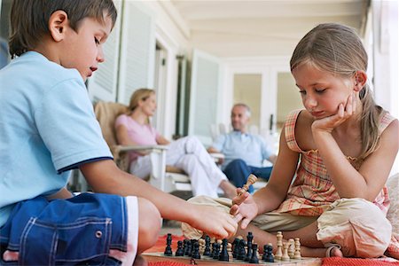 simsearch:693-03309303,k - Brother and sister (7-9) playing chess on porch, parents in background Stock Photo - Premium Royalty-Free, Code: 693-03304734