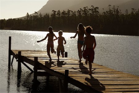 Four children (7-9) running down dock by lake, back view. Stock Photo - Premium Royalty-Free, Code: 693-03304767