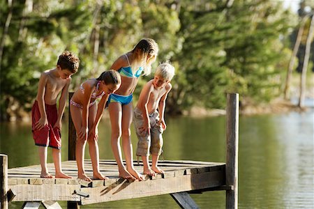 simsearch:693-03309308,k - Four children (7-9) in swimwear, standing on dock by lake. Stock Photo - Premium Royalty-Free, Code: 693-03304768