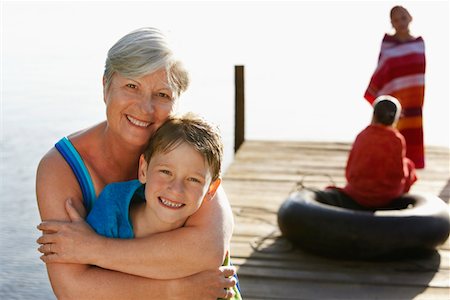 simsearch:693-03304775,k - Senior woman hugging grandson (5-6) on dock, with two children (7-9) in background. Stock Photo - Premium Royalty-Free, Code: 693-03304774