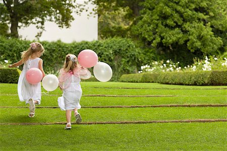 Two young girls running in garden, holding balloons, back view Stock Photo - Premium Royalty-Free, Code: 693-03304876