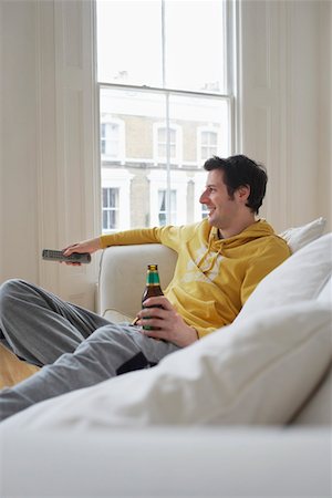 Man sitting on sofa, watching television and holding beer bottle Stock Photo - Premium Royalty-Free, Code: 693-03305084