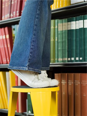 Young woman standing on stool, reaching for book, low section Stock Photo - Premium Royalty-Free, Code: 693-03305172