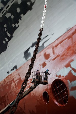 doca seca - Two men in cherry picker working at ship in dry dock, low angle view Foto de stock - Royalty Free Premium, Número: 693-03305279