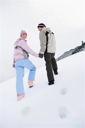 Couple walking up snow-covered hill, back view, low angle view Stock Photo - Premium Royalty-Free, Code: 693-03305345