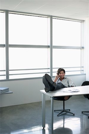 Business man using mobile phone sitting at office desk with feet up Stock Photo - Premium Royalty-Free, Code: 693-03305473