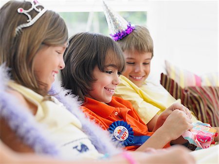 simsearch:693-03309303,k - Three children (7-12) sitting on sofa watching one open birthday present Stock Photo - Premium Royalty-Free, Code: 693-03305657