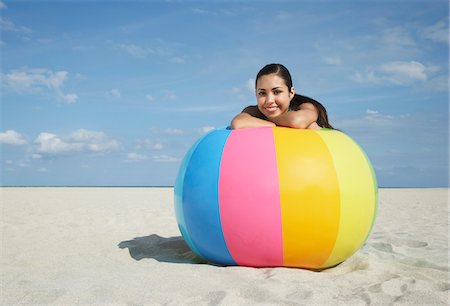 Teenage girl (16-17) sitting behind beach ball on beach, portrait Stock Photo - Premium Royalty-Free, Code: 693-03305809