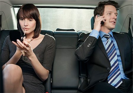 Couple at back seat of car, woman applying make-up, man using mobile phone Stock Photo - Premium Royalty-Free, Code: 693-03306317