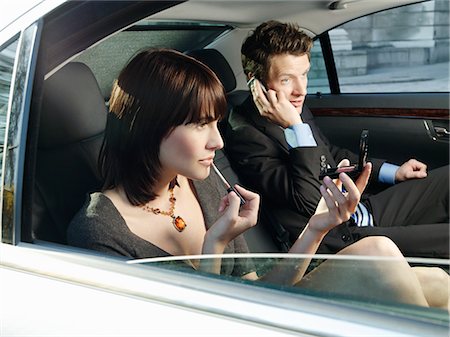 Couple at back seat of car, woman applying make-up, man using mobile phone Stock Photo - Premium Royalty-Free, Code: 693-03306318