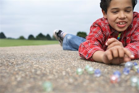 Boy (7-9) playing marbles, lying in playground Stock Photo - Premium Royalty-Free, Code: 693-03306998