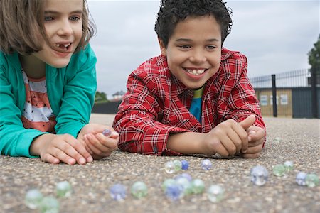 Boy and girl (7-9) playing marbles, lying in playground Stock Photo - Premium Royalty-Free, Code: 693-03306999