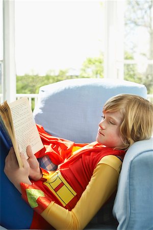 Young boy (7-9) sitting in armchair reading, wearing superhero costume, side view Foto de stock - Sin royalties Premium, Código: 693-03307205