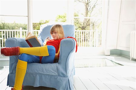 Young boy (7-9) sitting in armchair reading, wearing superhero costume Stock Photo - Premium Royalty-Free, Code: 693-03307203