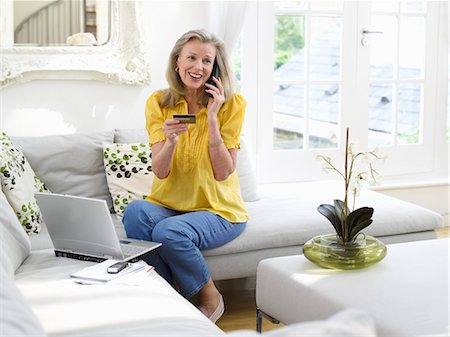 Woman holding credit card using phone in living room, elevated view Stock Photo - Premium Royalty-Free, Code: 693-03307281