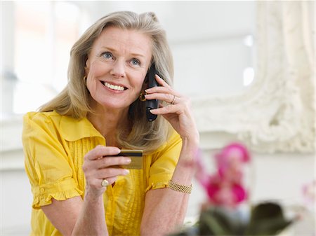 Woman holding credit card using phone in living room, portrait Stock Photo - Premium Royalty-Free, Code: 693-03307282