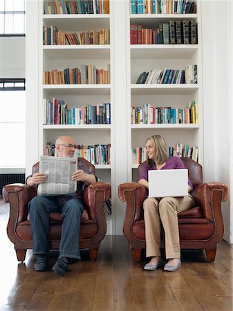 Couple assis dans les fauteuils, journal de lecture homme, femme utilisant un ordinateur portable Photographie de stock - Premium Libres de Droits, Code: 693-03307610