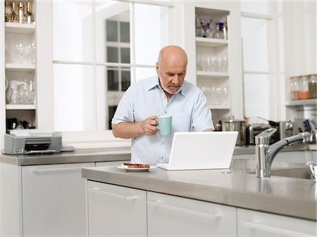 simsearch:693-03311596,k - Homme d'âge mûr dans la cuisine, à l'aide d'ordinateur portable et portefeuille café tasse Photographie de stock - Premium Libres de Droits, Code: 693-03307620