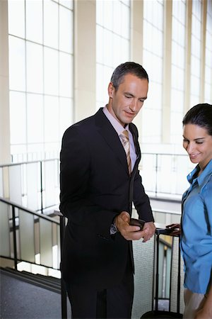 Business man showing woman mobile phone in airport lobby Stock Photo - Premium Royalty-Free, Code: 693-03307645