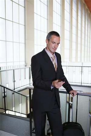 Business man sending text message in airport lobby Stock Photo - Premium Royalty-Free, Code: 693-03307646