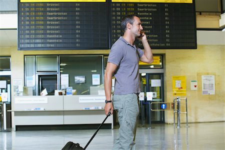 Traveller using mobile phone in front of flight status board in airport Stock Photo - Premium Royalty-Free, Code: 693-03307674