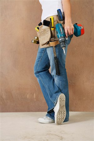 simsearch:693-03308062,k - Woman with toolbelt and drill leaning against wall, low section Fotografie stock - Premium Royalty-Free, Codice: 693-03308057