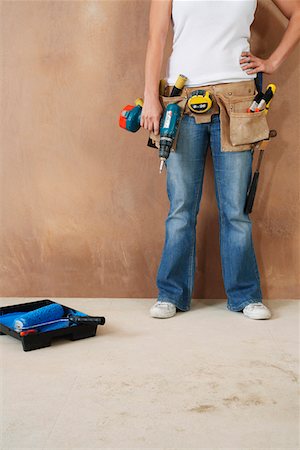 simsearch:693-03308062,k - Woman with toolbelt and drill leaning against wall, low section Fotografie stock - Premium Royalty-Free, Codice: 693-03308059