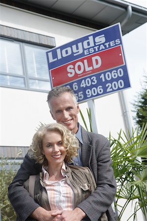 simsearch:693-03308239,k - Couple embracing outside new home with sold sign, portrait Fotografie stock - Premium Royalty-Free, Codice: 693-03308234