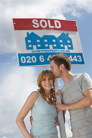 simsearch:693-03308239,k - Couple holding sold sign against sky, man kissing woman Fotografie stock - Premium Royalty-Free, Codice: 693-03308291