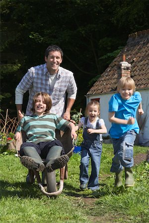 simsearch:693-03308429,k - Father and children (5-9) racing with wheelbarrow outside cottage Stock Photo - Premium Royalty-Free, Code: 693-03308354