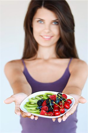 Young woman holding plate of fruit, focus on foreground Stock Photo - Premium Royalty-Free, Code: 693-03308605
