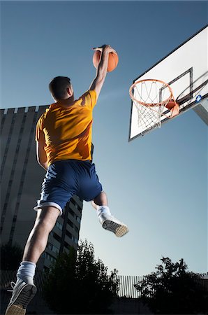 Young man with basketball jumping towards hoop, mid-air Stock Photo - Premium Royalty-Free, Code: 693-03309168