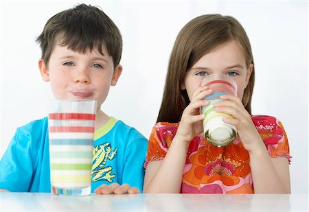 Boy and girl (5-6) sitting at table, drinking milk from colourful glasses, portrait Stock Photo - Premium Royalty-Free, Code: 693-03309176